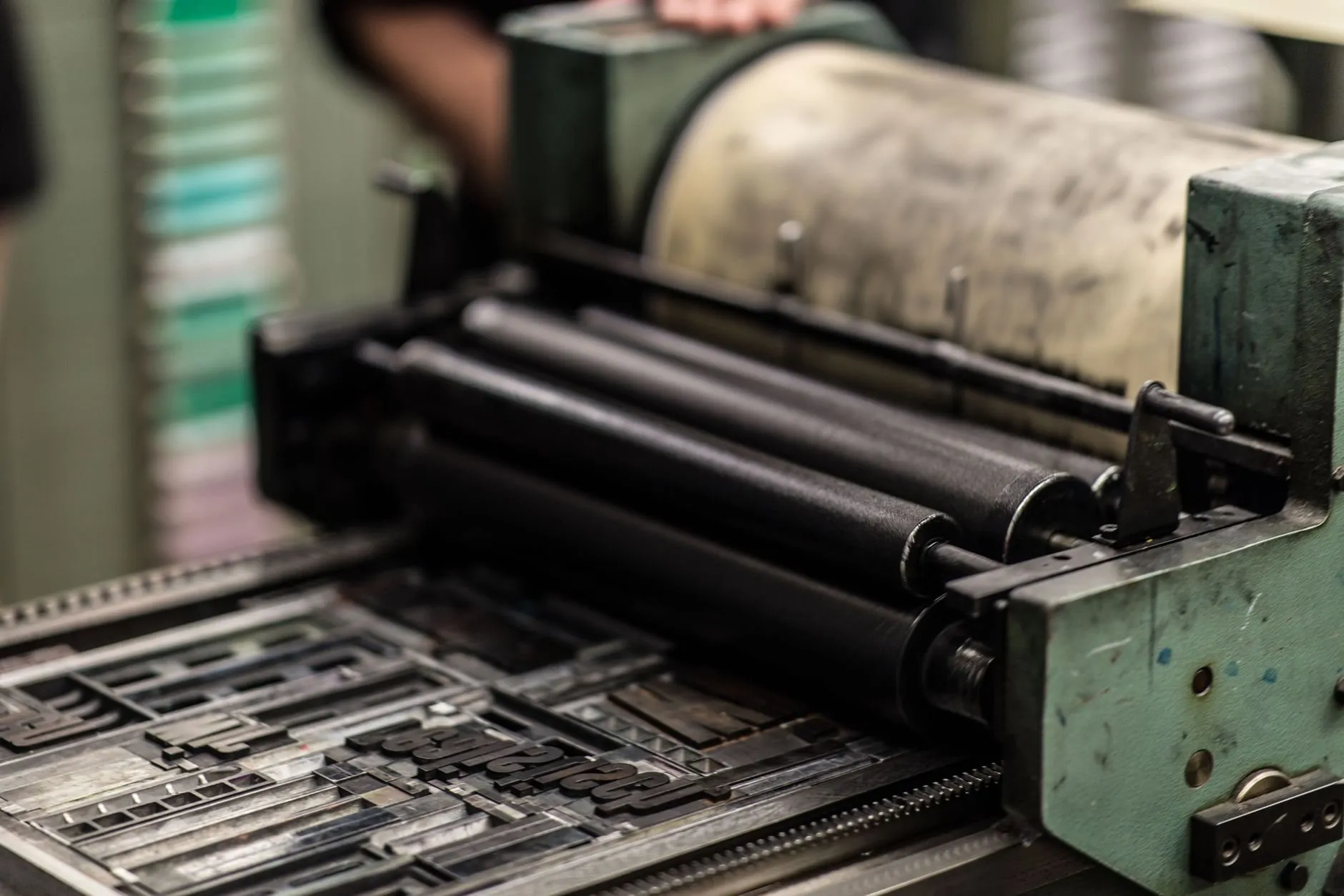 Inked black rollers of a small proofing press running over a forme of metal type